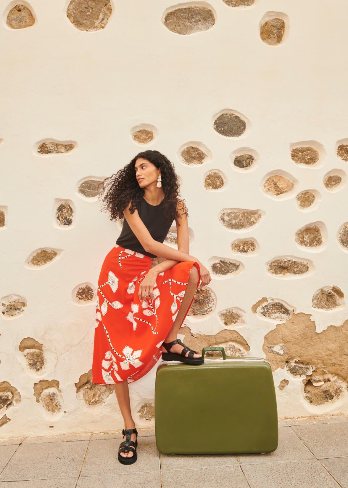 Woman in linen skirt resting foot on green suitcase